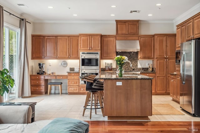 kitchen with a center island, stainless steel appliances, visible vents, dark stone countertops, and ventilation hood