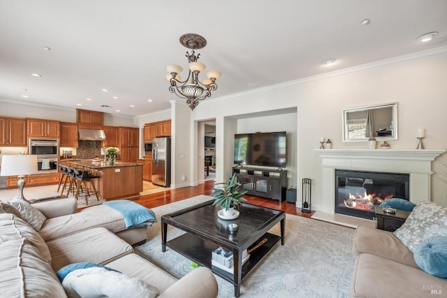 living room featuring light wood-style floors, a glass covered fireplace, crown molding, and recessed lighting