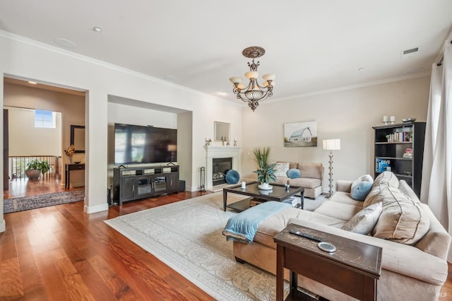 living area with a chandelier, wood finished floors, visible vents, ornamental molding, and a glass covered fireplace