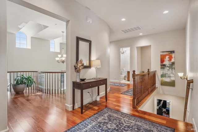 hallway featuring a chandelier, visible vents, an upstairs landing, and wood finished floors