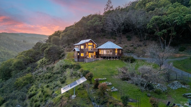 back of property at dusk featuring metal roof, a lawn, a deck, and a wooded view