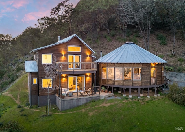 back of house at dusk with metal roof, a lawn, a patio area, and a balcony