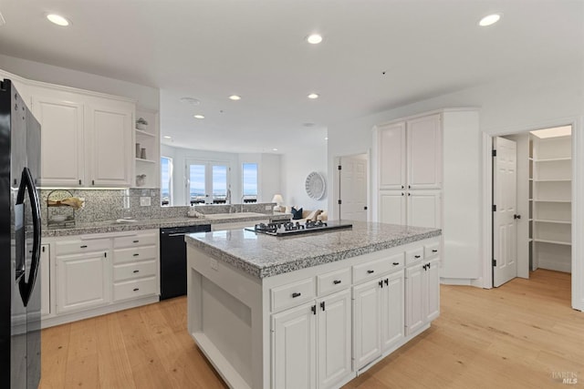 kitchen with tile counters, light wood-style floors, a kitchen island, black appliances, and open shelves