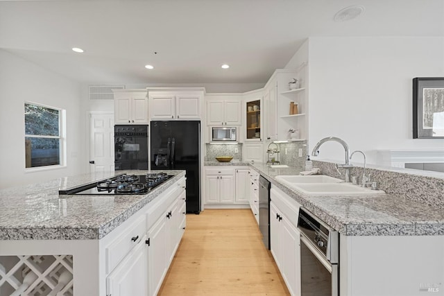 kitchen featuring light wood finished floors, a kitchen island, a sink, black appliances, and backsplash