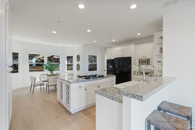 kitchen with a sink, light wood finished floors, black appliances, and open shelves