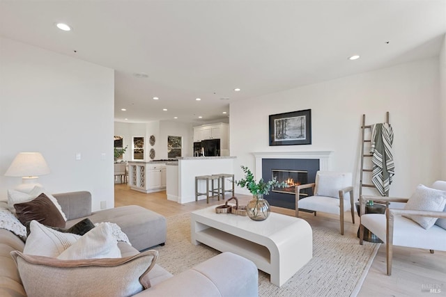 living area featuring light wood-type flooring, a glass covered fireplace, and recessed lighting