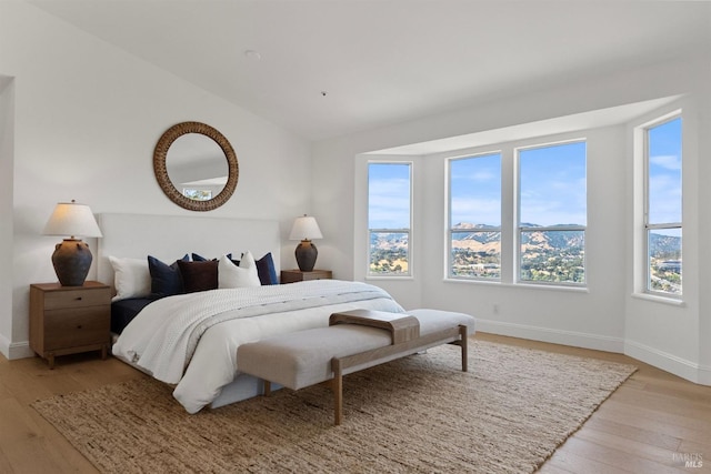 bedroom with vaulted ceiling, light wood-style flooring, and baseboards