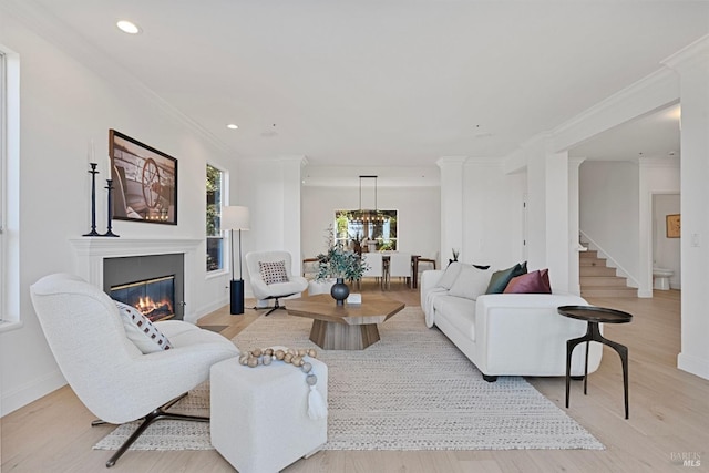 living room with stairs, a glass covered fireplace, ornamental molding, and wood finished floors