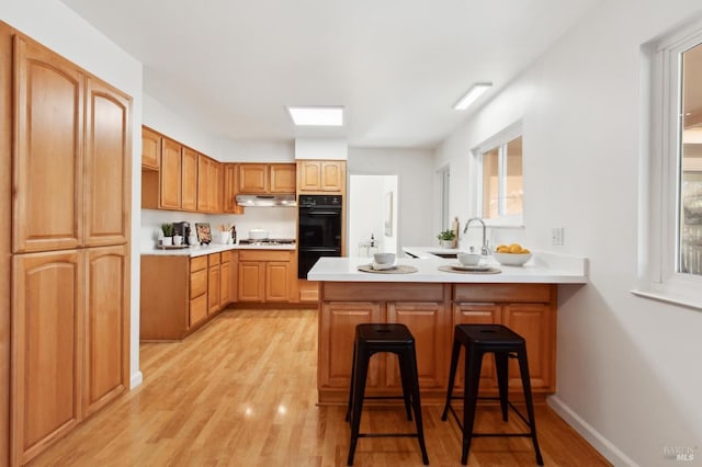 kitchen featuring stainless steel gas cooktop, dobule oven black, a sink, a peninsula, and under cabinet range hood