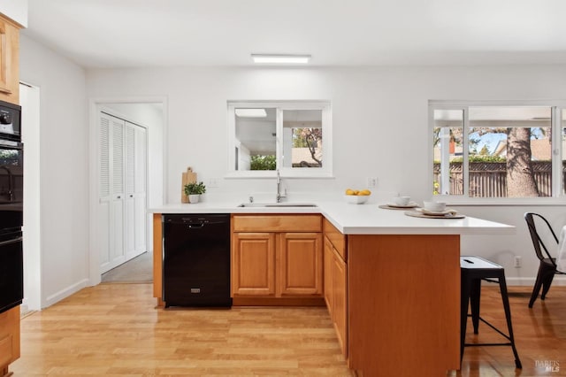 kitchen featuring dishwasher, a breakfast bar, a peninsula, light countertops, and a sink