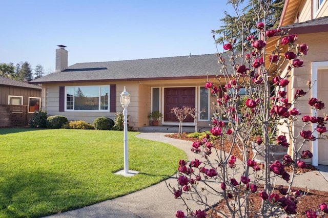 single story home with a shingled roof, a chimney, and a front yard