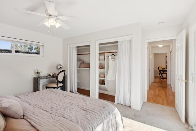 bedroom featuring ceiling fan, light colored carpet, and multiple closets