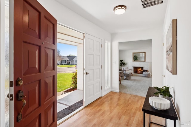 foyer entrance with a brick fireplace, visible vents, and light wood-style floors