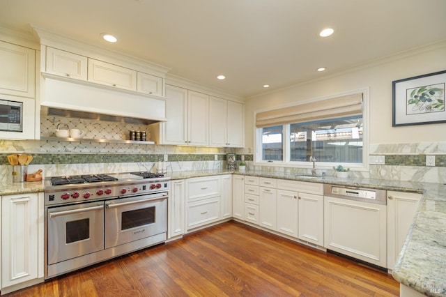 kitchen featuring dark wood-style floors, custom range hood, appliances with stainless steel finishes, light stone counters, and a sink