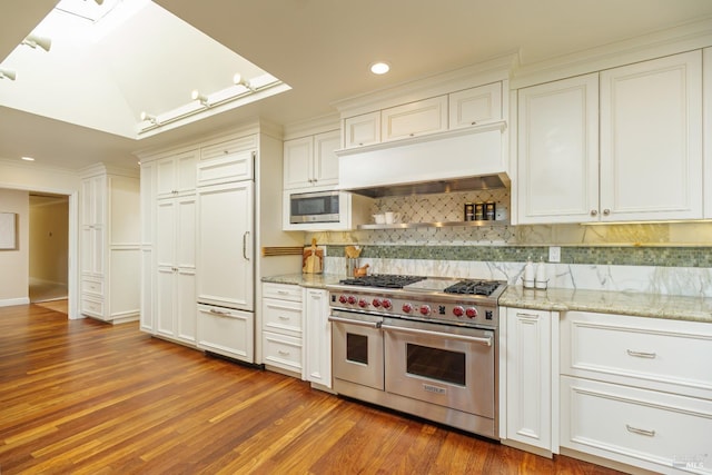 kitchen featuring light stone counters, a skylight, tasteful backsplash, wood finished floors, and built in appliances