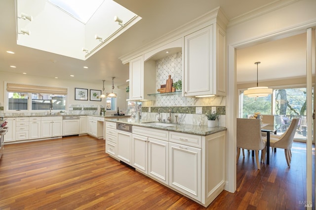 kitchen with white cabinets, wood finished floors, a sink, light stone countertops, and backsplash