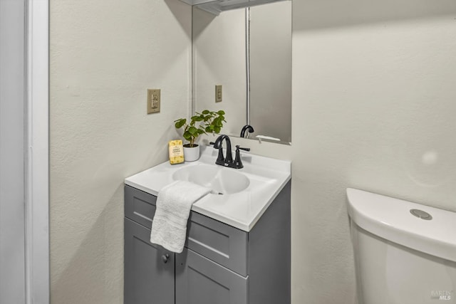 bathroom featuring toilet, a textured wall, and vanity