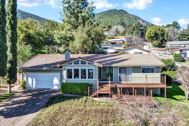 view of front of home with a tile roof, a chimney, a deck with mountain view, a garage, and driveway