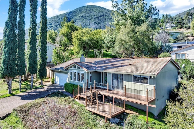 back of house featuring aphalt driveway, a tile roof, a chimney, a deck with mountain view, and a garage