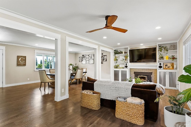 living room with baseboards, dark wood finished floors, ceiling fan, crown molding, and a fireplace