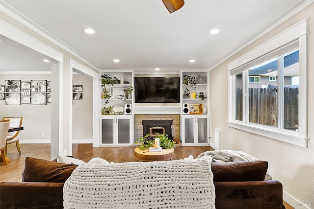 living area featuring recessed lighting, wood finished floors, baseboards, ornamental molding, and a brick fireplace