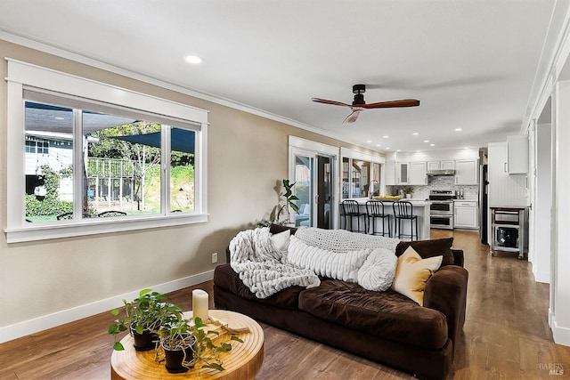 living area with ceiling fan, crown molding, baseboards, and wood finished floors