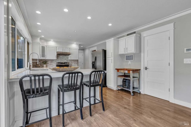 kitchen with appliances with stainless steel finishes, light wood-style floors, white cabinetry, a sink, and a peninsula