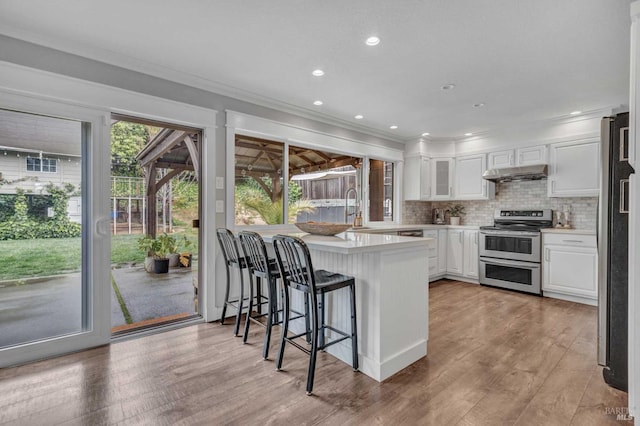 kitchen featuring a peninsula, range with two ovens, white cabinets, and under cabinet range hood