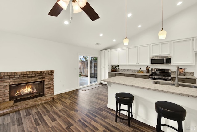 kitchen featuring a sink, decorative light fixtures, dark wood finished floors, appliances with stainless steel finishes, and a breakfast bar area