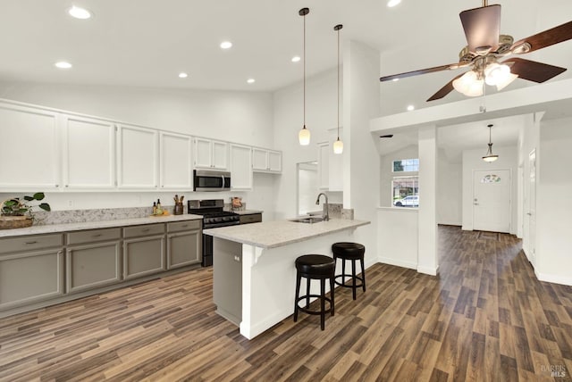 kitchen featuring dark wood-style floors, gray cabinetry, a sink, appliances with stainless steel finishes, and a kitchen breakfast bar