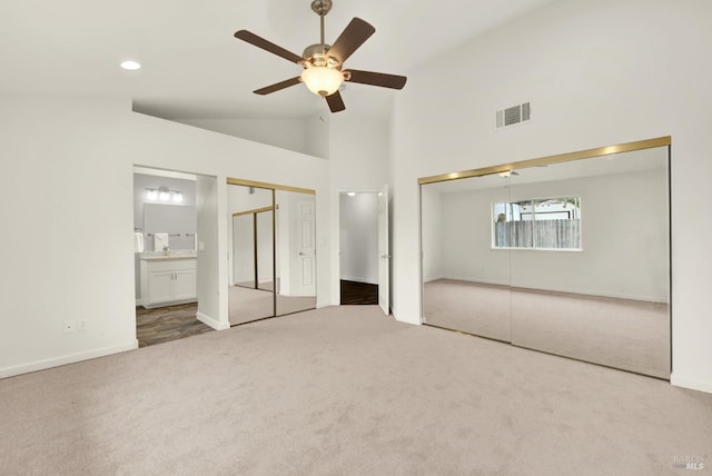 unfurnished bedroom featuring visible vents, carpet floors, high vaulted ceiling, multiple closets, and connected bathroom