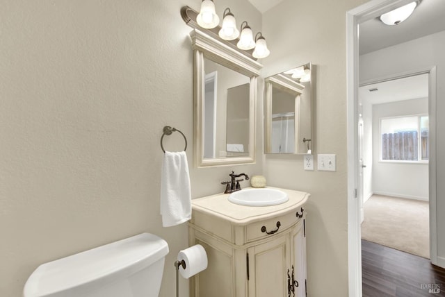 bathroom with vanity, toilet, wood finished floors, and baseboards