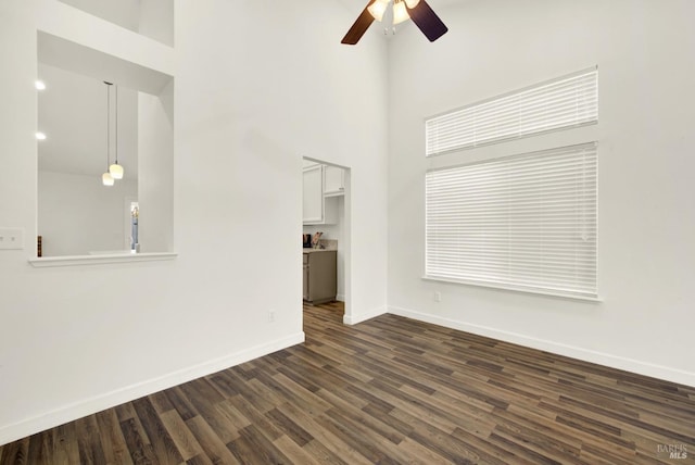 unfurnished living room with dark wood finished floors, ceiling fan, baseboards, and a towering ceiling