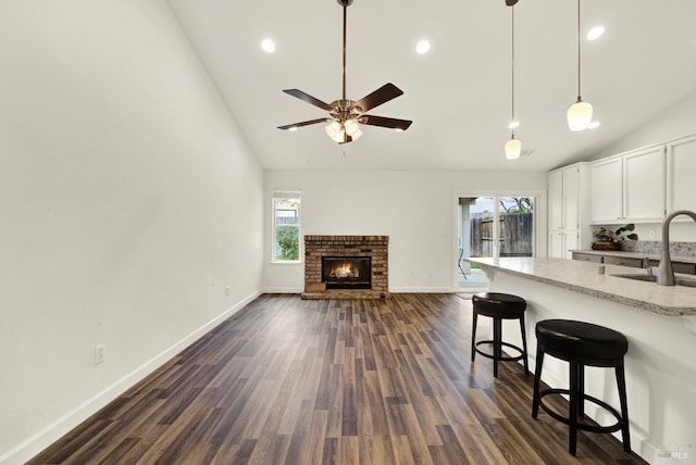 kitchen with light stone counters, white cabinetry, a fireplace, a sink, and a kitchen bar