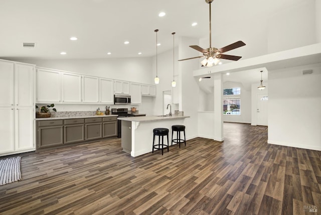 kitchen featuring a breakfast bar, gray cabinetry, dark wood-style floors, appliances with stainless steel finishes, and light countertops