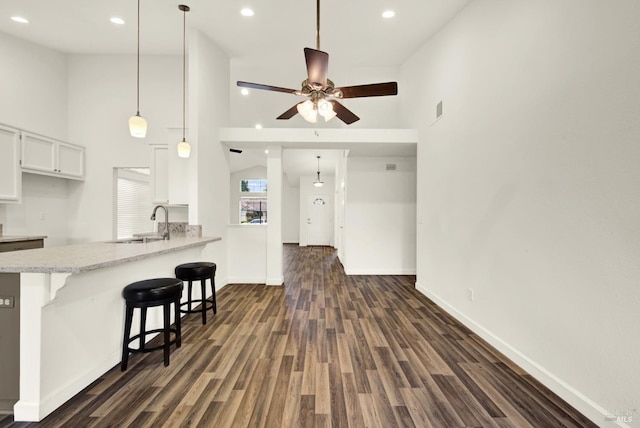 kitchen with a peninsula, a kitchen breakfast bar, dark wood-style floors, white cabinets, and a sink