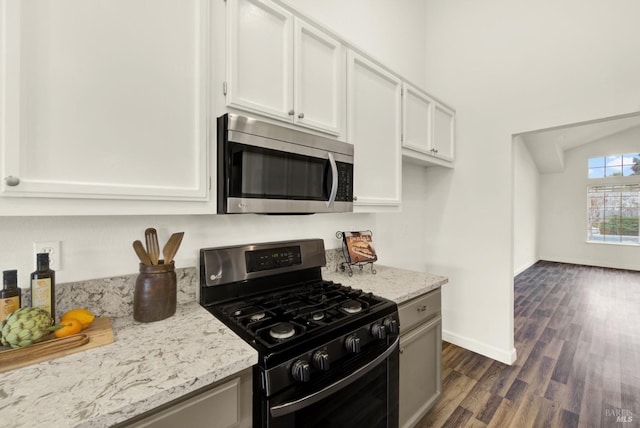 kitchen with light stone counters, dark wood-style floors, white cabinetry, stainless steel appliances, and baseboards