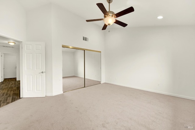 unfurnished bedroom with carpet flooring, visible vents, a closet, and high vaulted ceiling