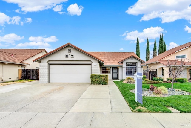 mediterranean / spanish home featuring fence, a tiled roof, concrete driveway, a front yard, and an attached garage