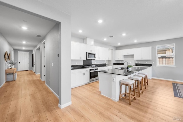 kitchen with dark countertops, appliances with stainless steel finishes, white cabinets, and light wood finished floors