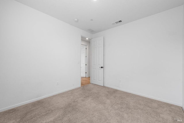 spare room featuring baseboards, visible vents, and light carpet