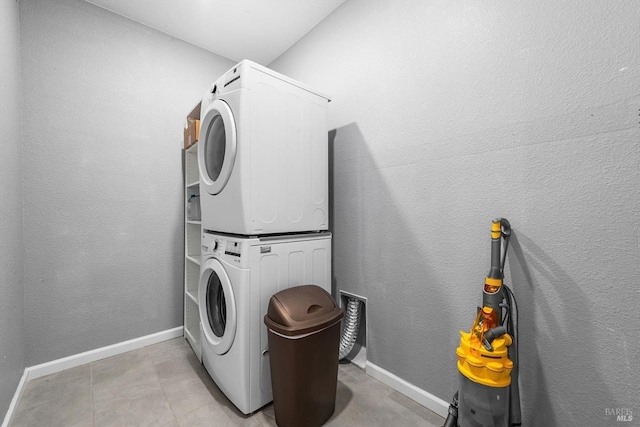 laundry room with stacked washer / dryer, baseboards, laundry area, a textured wall, and light tile patterned flooring