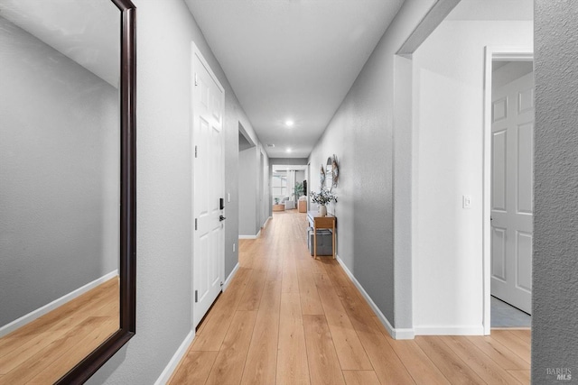 hallway with baseboards, light wood-style floors, and a textured wall