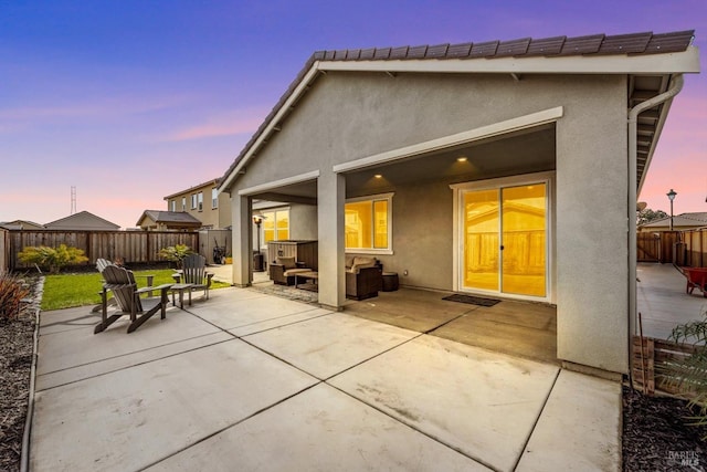 back of house at dusk featuring stucco siding, an outdoor hangout area, a fenced backyard, and a patio area