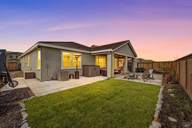 back of house at dusk with a patio, central AC unit, a fenced backyard, stucco siding, and a lawn