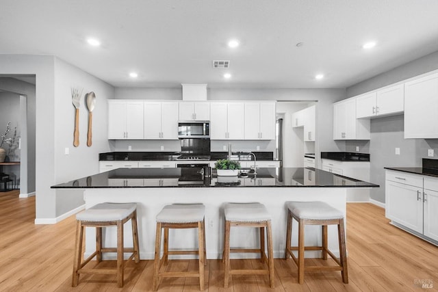 kitchen with stainless steel microwave, visible vents, light wood-style flooring, and white cabinetry