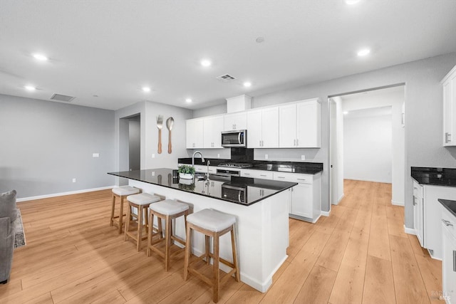 kitchen with a breakfast bar area, visible vents, a sink, light wood-style floors, and stainless steel microwave