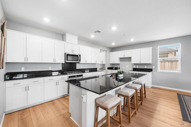 kitchen featuring a sink, stainless steel microwave, visible vents, and light wood-style flooring