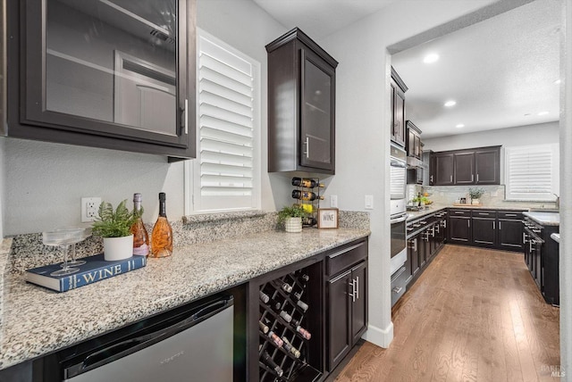 kitchen with dishwasher, glass insert cabinets, light stone counters, dark brown cabinets, and light wood-style floors