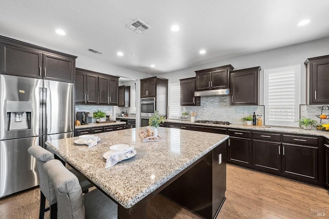 kitchen with light wood-style flooring, light stone counters, stainless steel appliances, and a center island